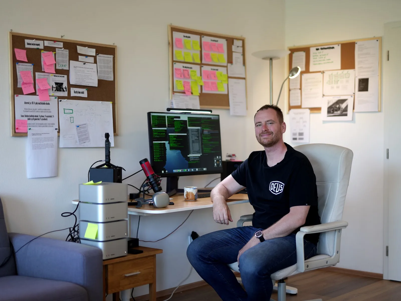 Jindřich Fáborský ve své pracovně, vedle něj stoh Maců na lokální běh AI modelů